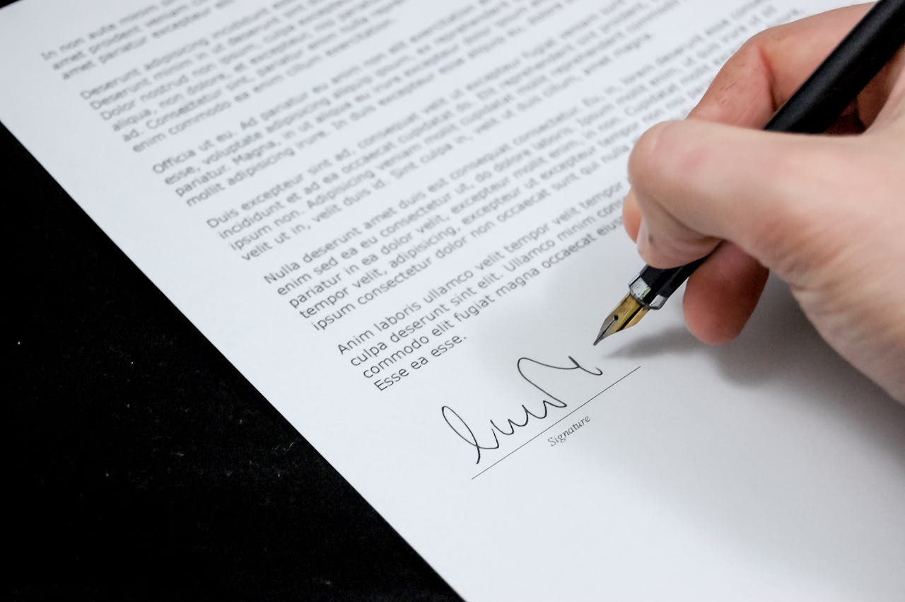 services-01 Close-up of a hand signing a formal document with a fountain pen, indicating agreement.